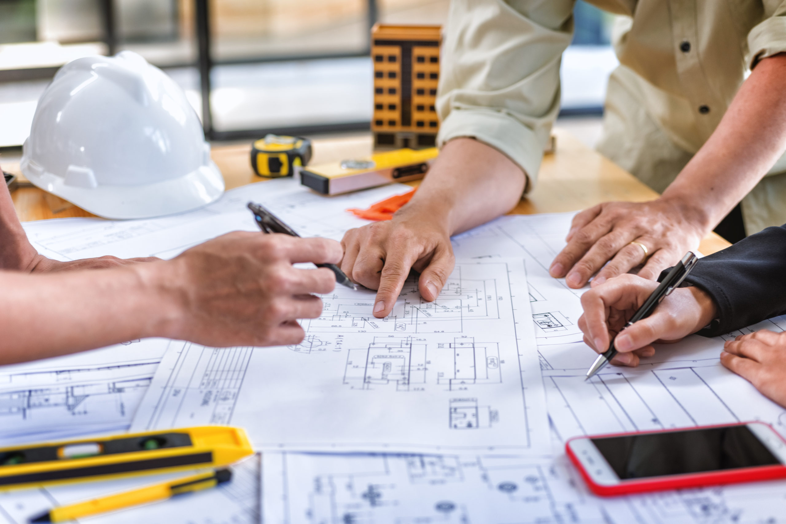 Team engineer meeting for colleagues discussing and checks construction blueprints on new project at desk in office.